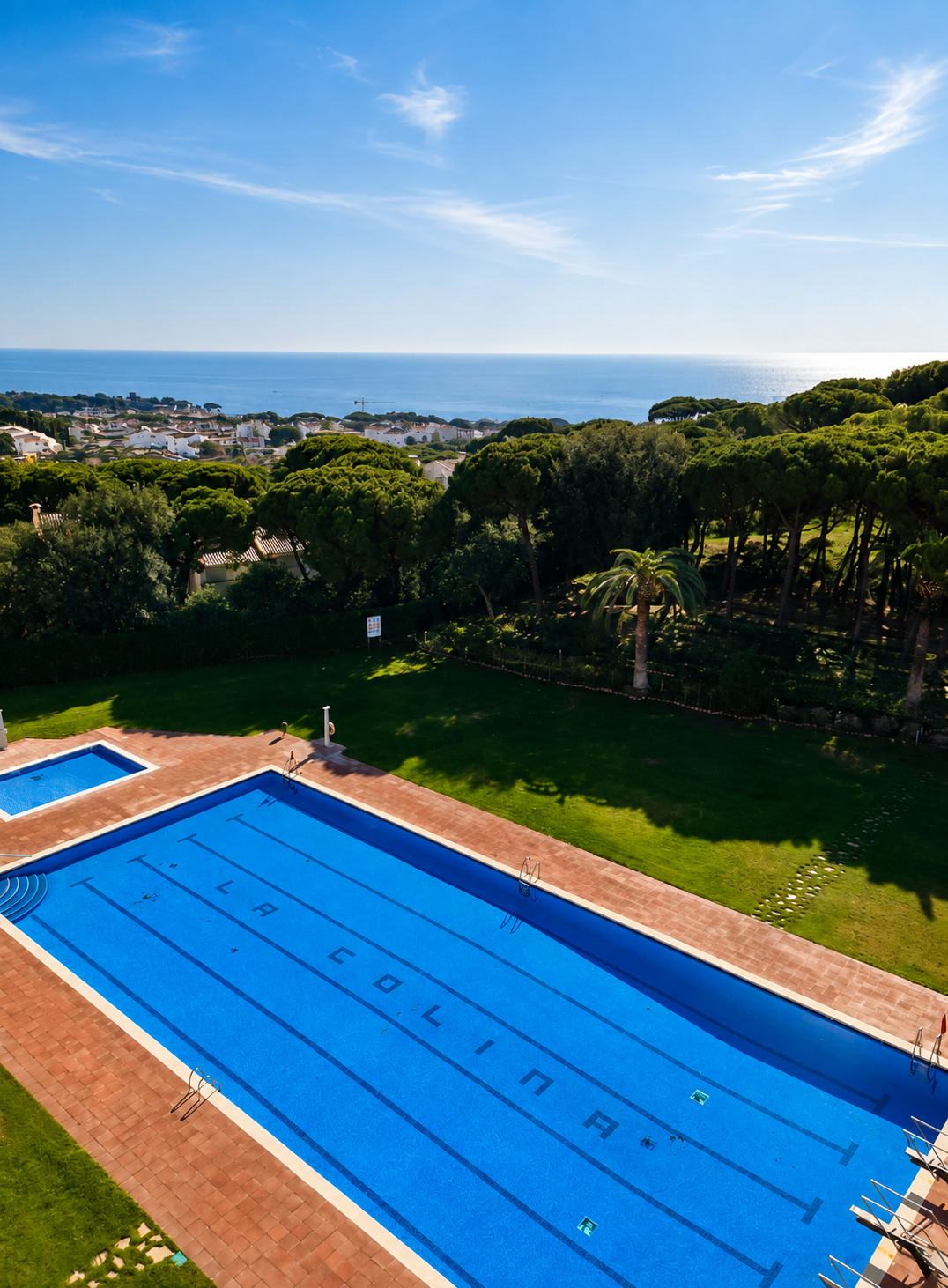 La piscine de la résidence entourée de pelouse et de pins, la mer à l'horizon